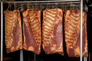 Racks of smoked pork ribs hanging in a smoker.