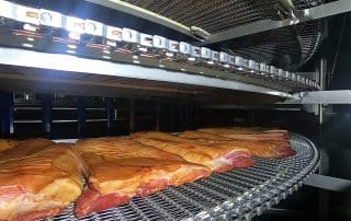 Pork belly smoking in an industrial smoker machine.